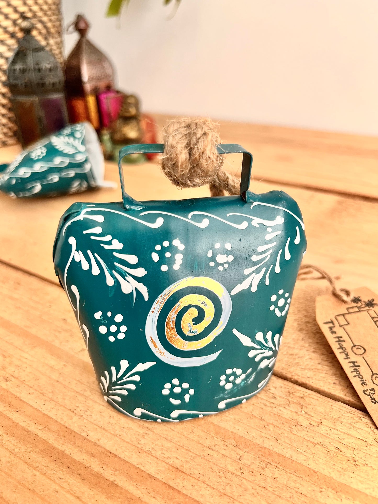 Hand painted traditional Indian hanging cow bell wind chime in blue colour with white floral feather painted detail and metallic swirl hand painted pattern handmade fair trade & ethically sourced with rustic jute twine hanging