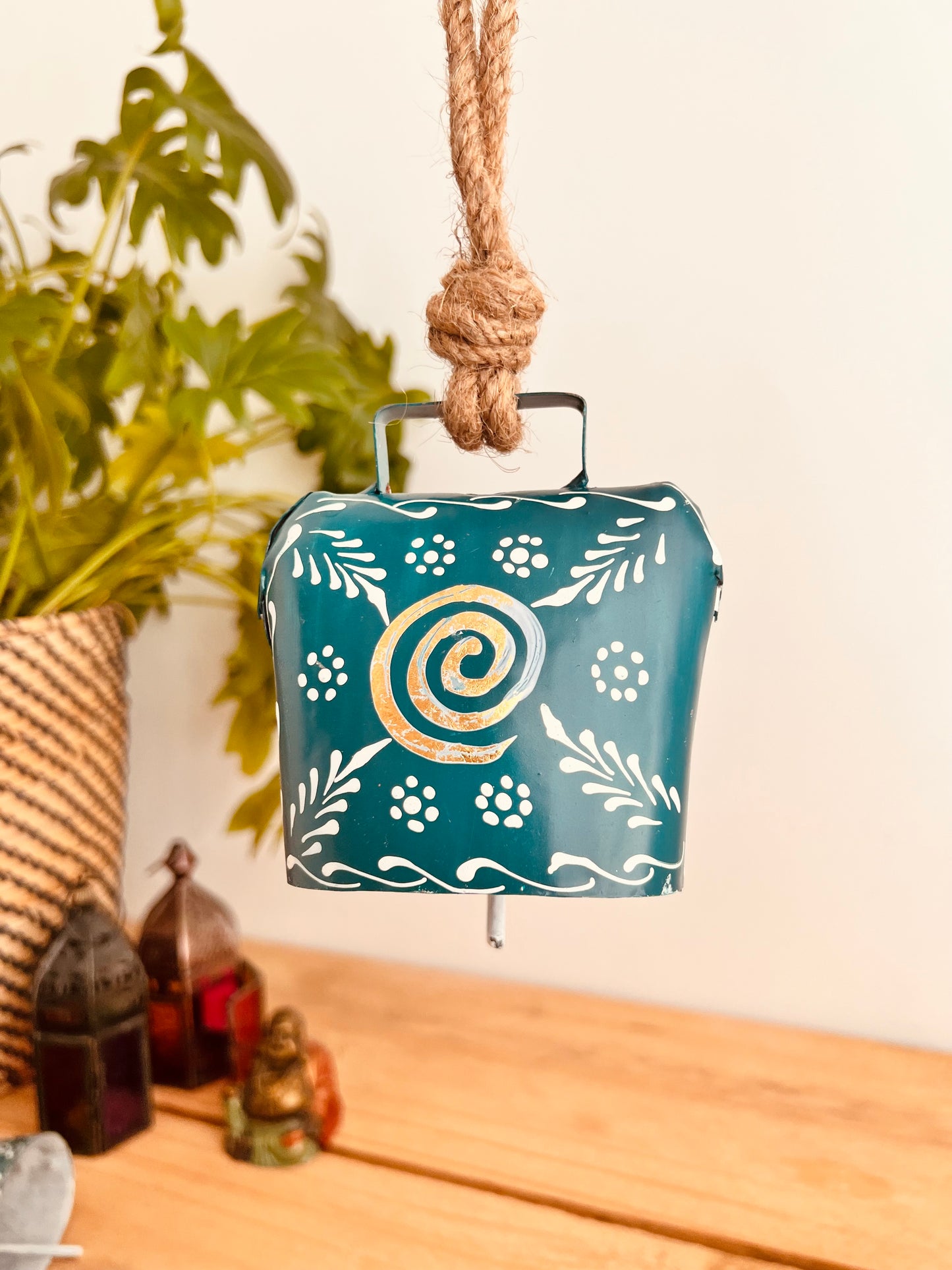 Hand painted traditional Indian hanging cow bell wind chime in blue colour with white floral feather painted detail and metallic swirl hand painted pattern handmade fair trade & ethically sourced with rustic jute twine hanging
