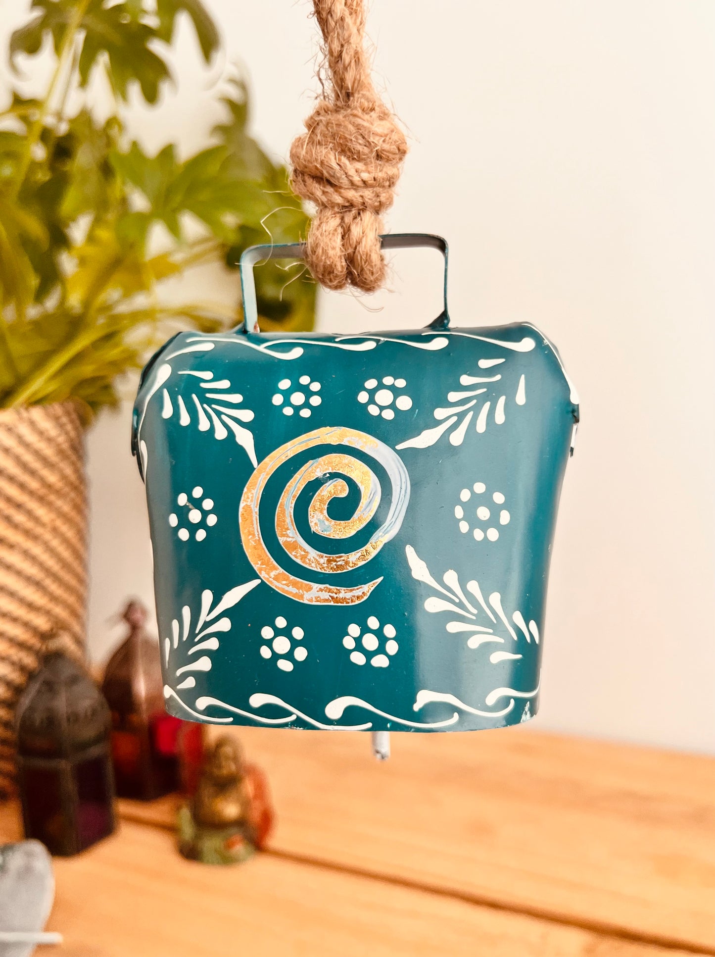 Hand painted traditional Indian hanging cow bell wind chime in blue colour with white floral feather painted detail and metallic swirl hand painted pattern handmade fair trade & ethically sourced with rustic jute twine hanging