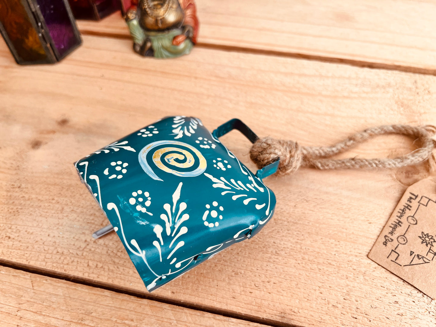 Hand painted traditional Indian hanging cow bell wind chime in blue colour with white floral feather painted detail and metallic swirl hand painted pattern handmade fair trade & ethically sourced with rustic jute twine hanging