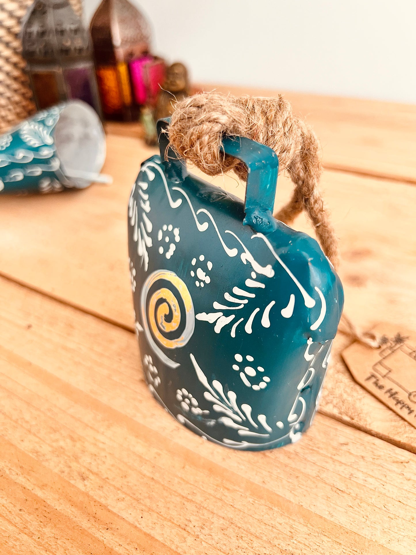 Hand painted traditional Indian hanging cow bell wind chime in blue colour with white floral feather painted detail and metallic swirl hand painted pattern handmade fair trade & ethically sourced with rustic jute twine hanging