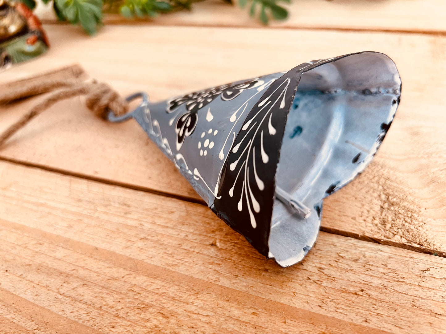 Hand-painted recycled metal bell in light grey with black and white floral patterns, hanging on rustic jute twine. Handmade, fair trade hippie boho decor.