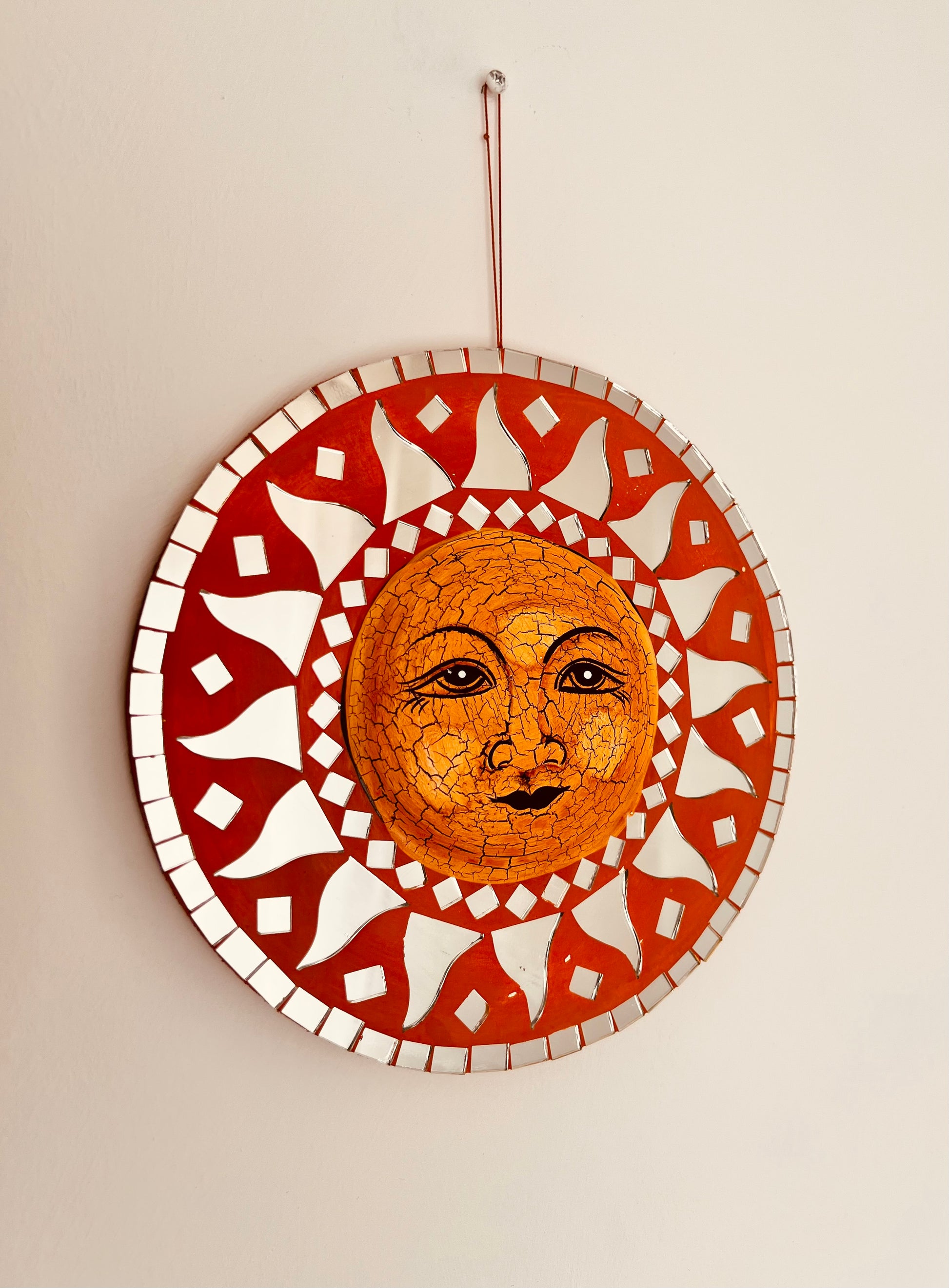 A circular mosaic wall hanging featuring a boho hippie sun face in the centre, surrounded by mosaic mirror tiles patterns, suspended with hanging loop 