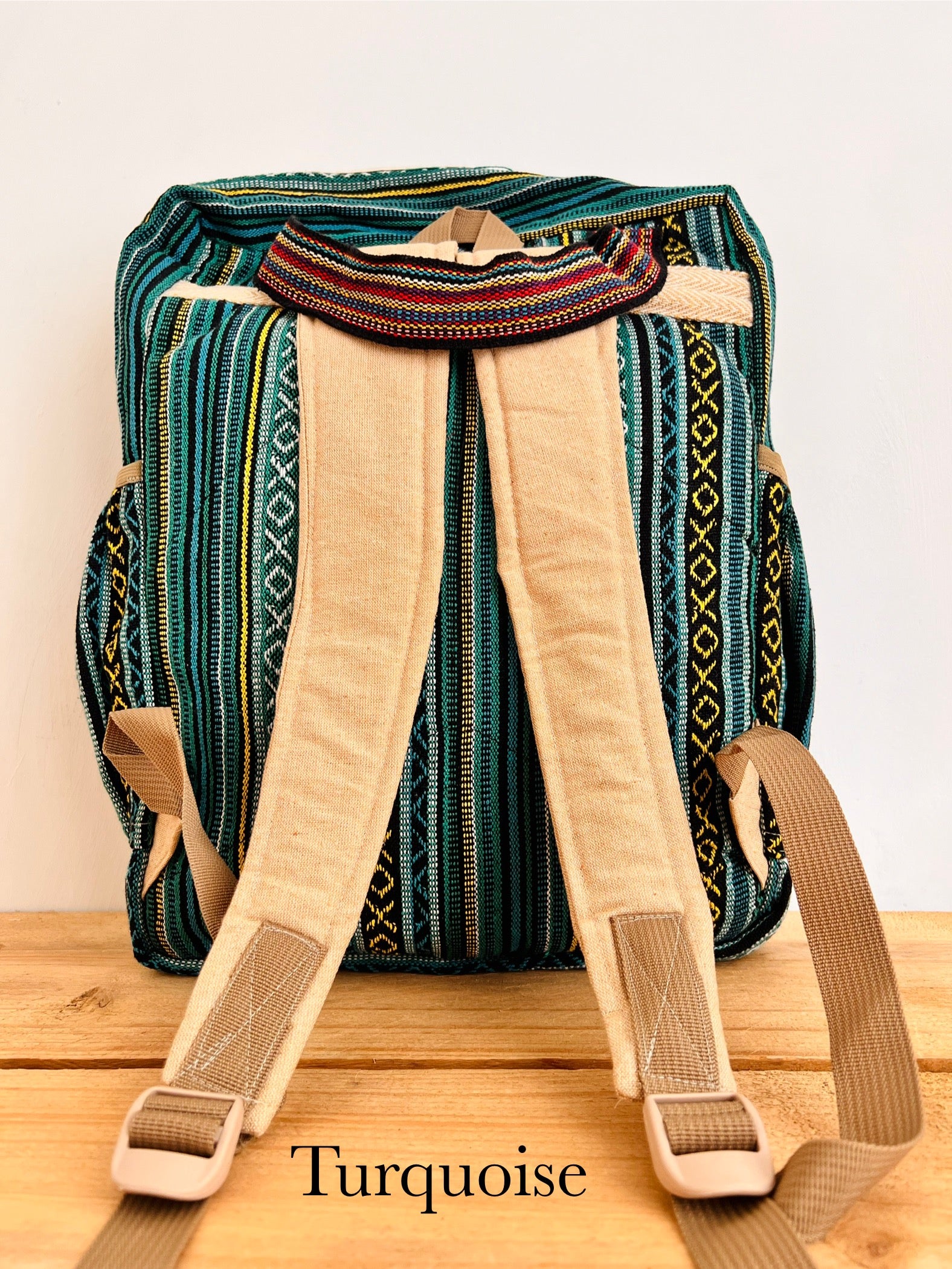 A woven backpack with a turquoise and green patterned body, beige padded shoulder straps, and a matching beige top handle, displayed on a wooden surface against a plain light background. The word 'Turquoise' is printed at the bottom.