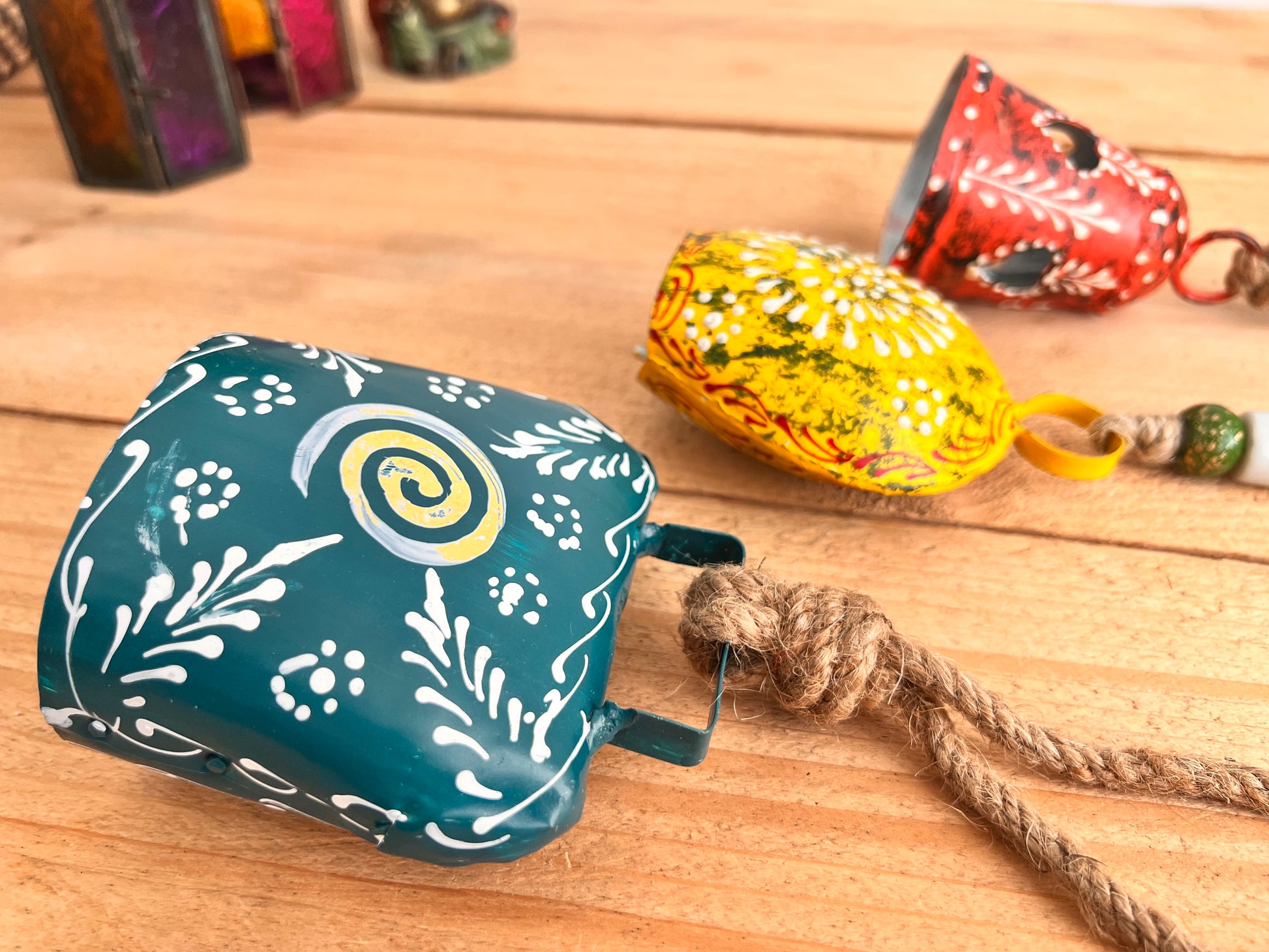 a set of three metal hand painted Indian hanging bells in three different sizes, jute twine hanging cow bell wind chimes in three mixed sizes, yellow, red & blue metal painted bells, handmade, fair trade & ethically sourced hippie boho home decor. 