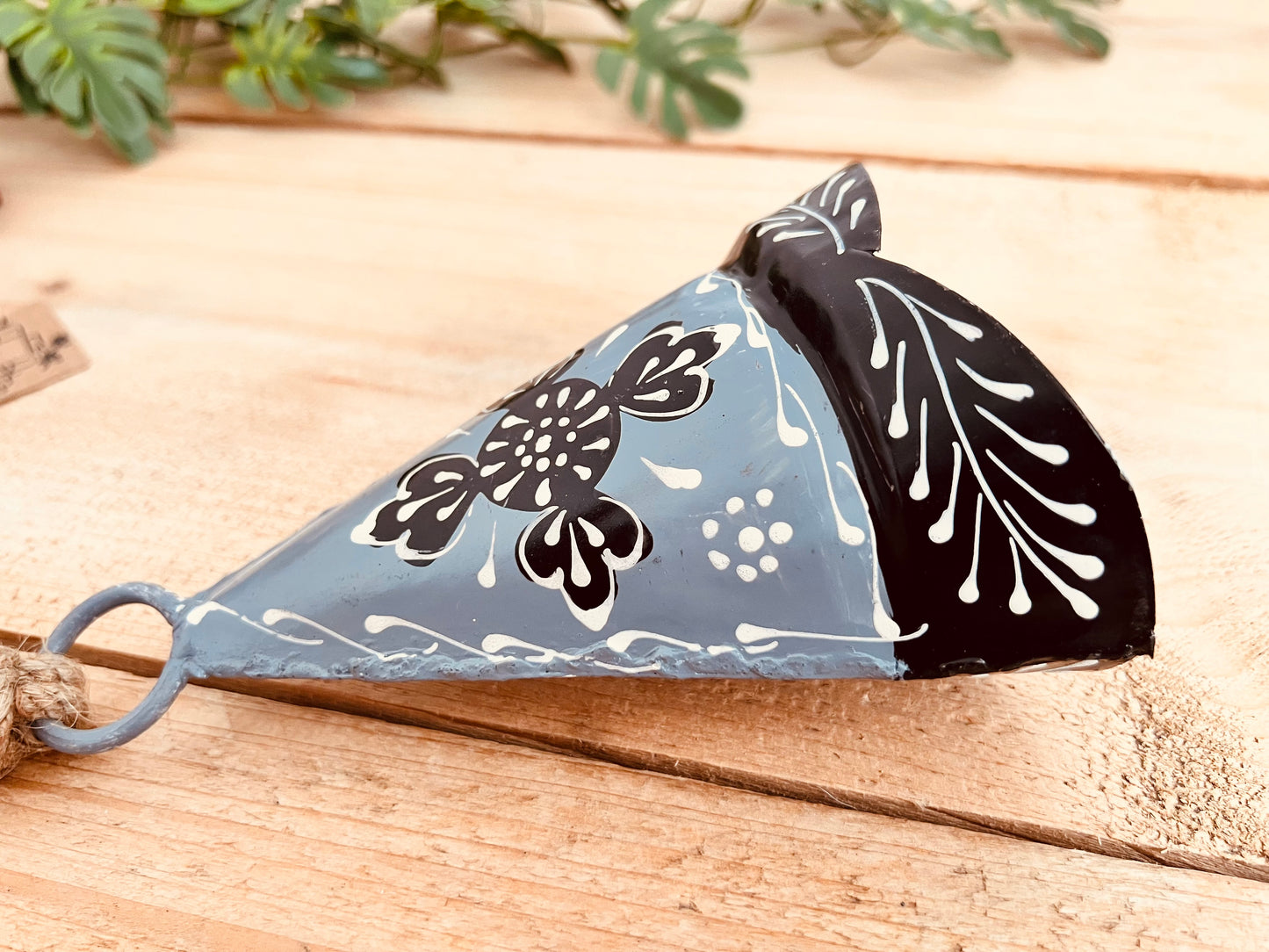 Hand-painted recycled metal bell in light grey with black and white floral patterns, hanging on rustic jute twine. Handmade, fair trade hippie boho decor.