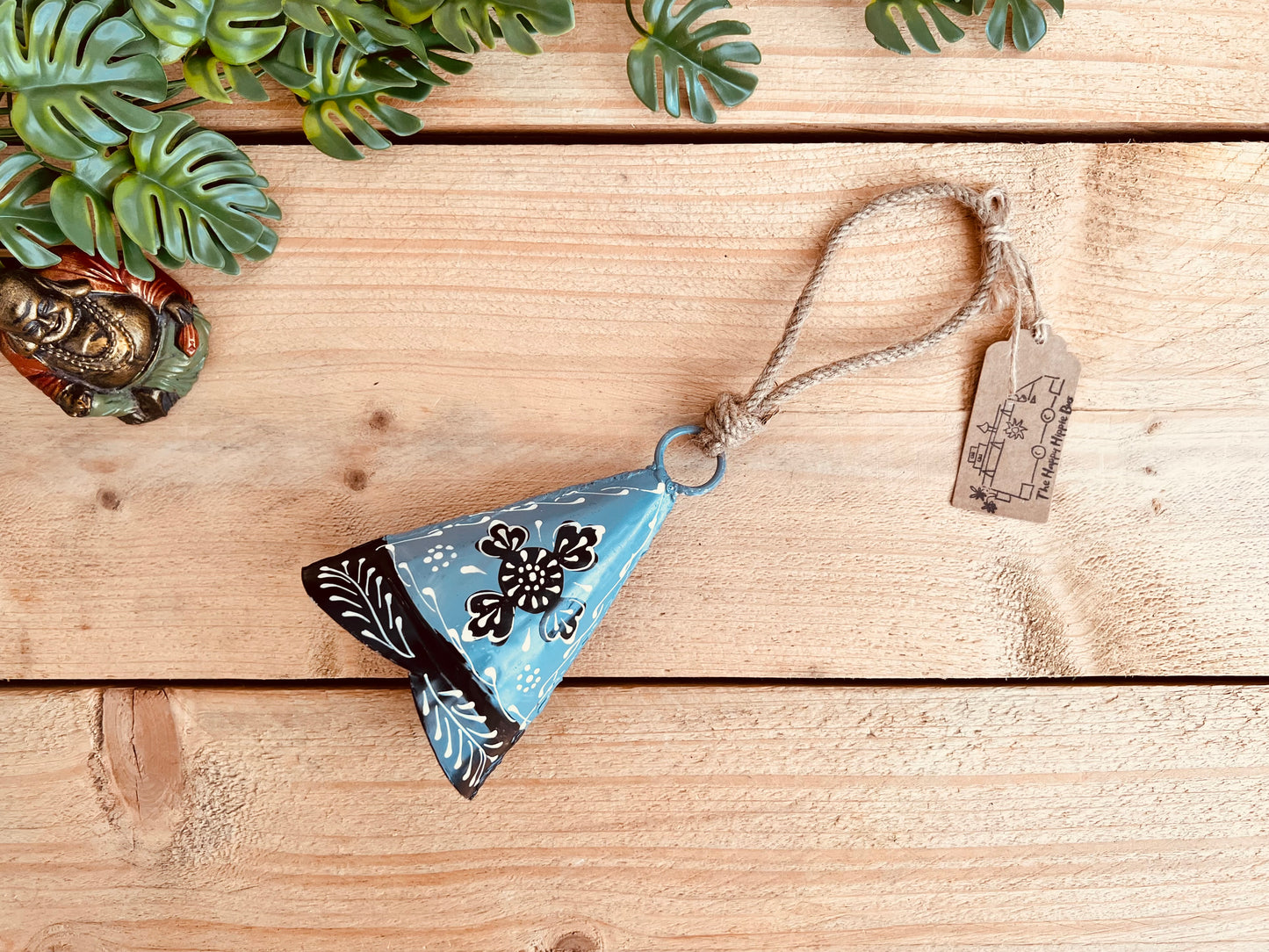 Hand-painted recycled metal bell in light grey with black and white floral patterns, hanging on rustic jute twine. Handmade, fair trade hippie boho decor.