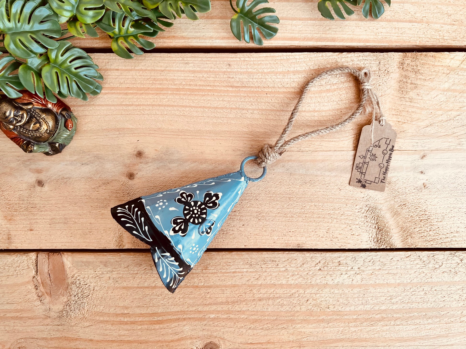 Hand-painted recycled metal bell in light grey with black and white floral patterns, hanging on rustic jute twine. Handmade, fair trade hippie boho decor.