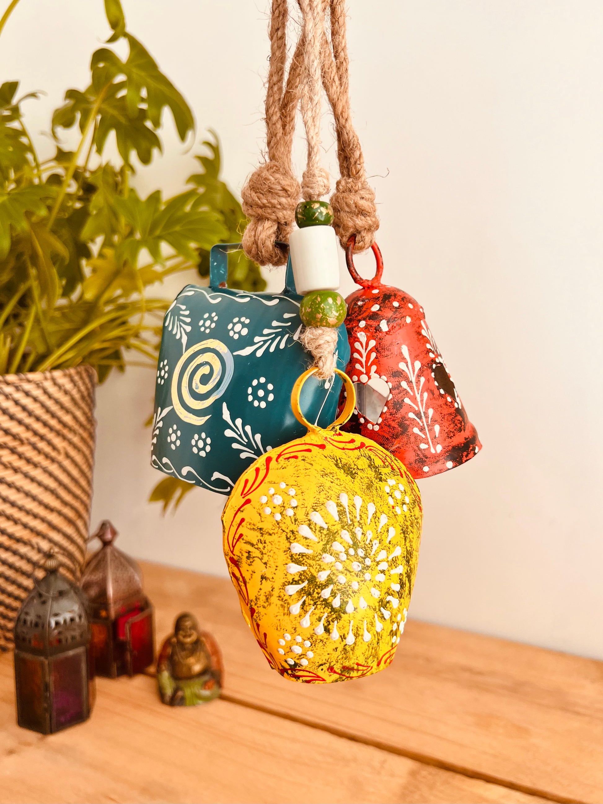 a set of three metal hand painted Indian hanging bells in three different sizes, jute twine hanging cow bell wind chimes in three mixed sizes, yellow, red & blue metal painted bells, handmade, fair trade & ethically sourced hippie boho home decor. 