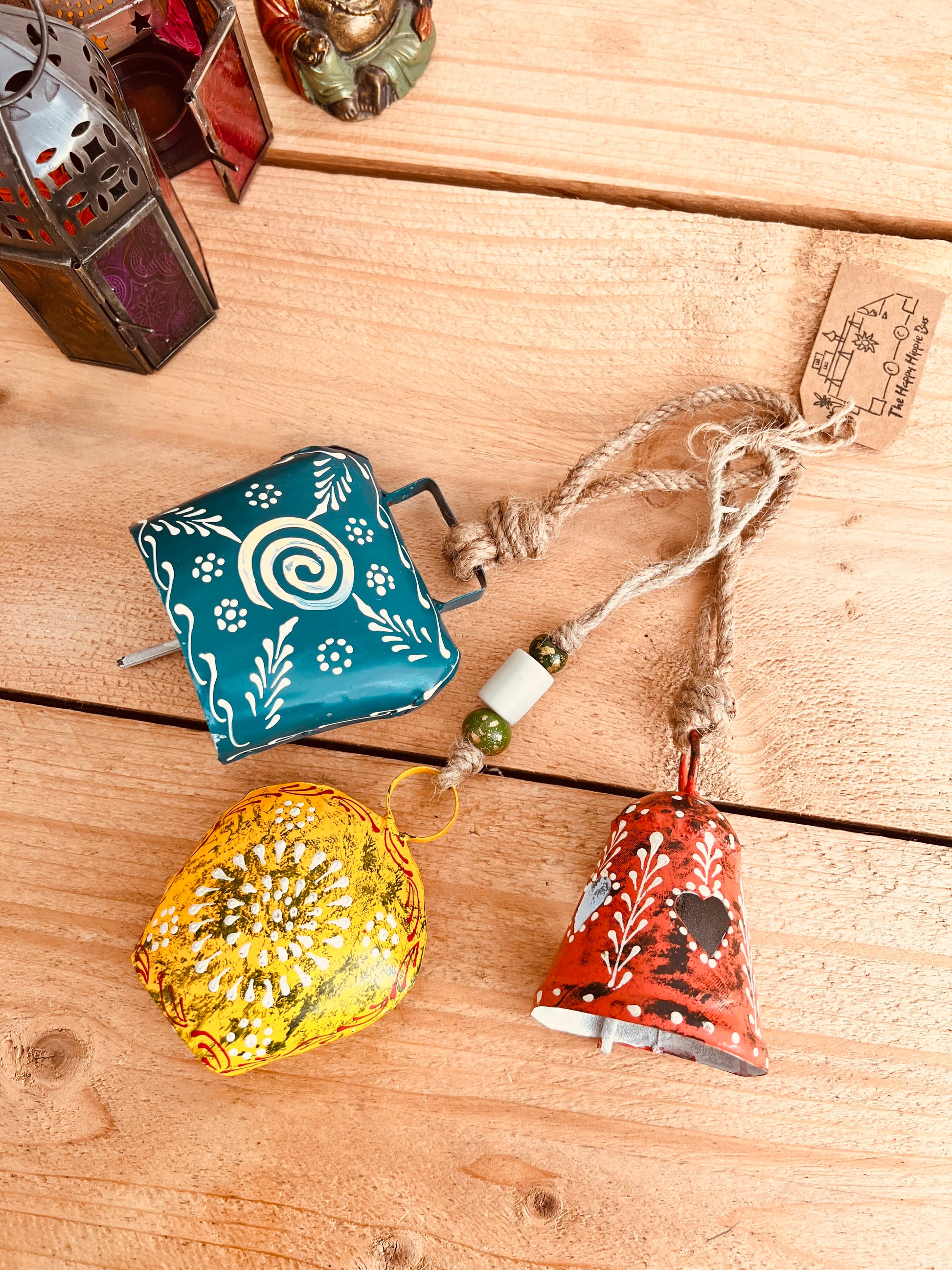a set of three metal hand painted Indian hanging bells in three different sizes, jute twine hanging cow bell wind chimes in three mixed sizes, yellow, red & blue metal painted bells, handmade, fair trade & ethically sourced hippie boho home decor. 