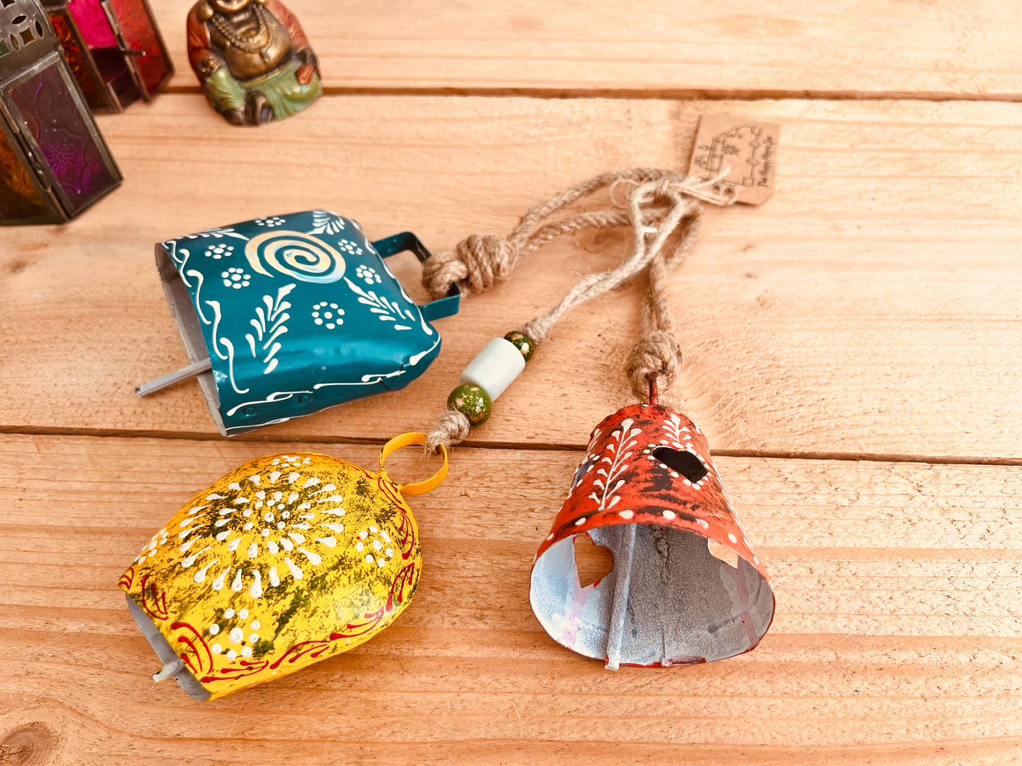 a set of three metal hand painted Indian hanging bells in three different sizes, jute twine hanging cow bell wind chimes in three mixed sizes, yellow, red & blue metal painted bells, handmade, fair trade & ethically sourced hippie boho home decor. 