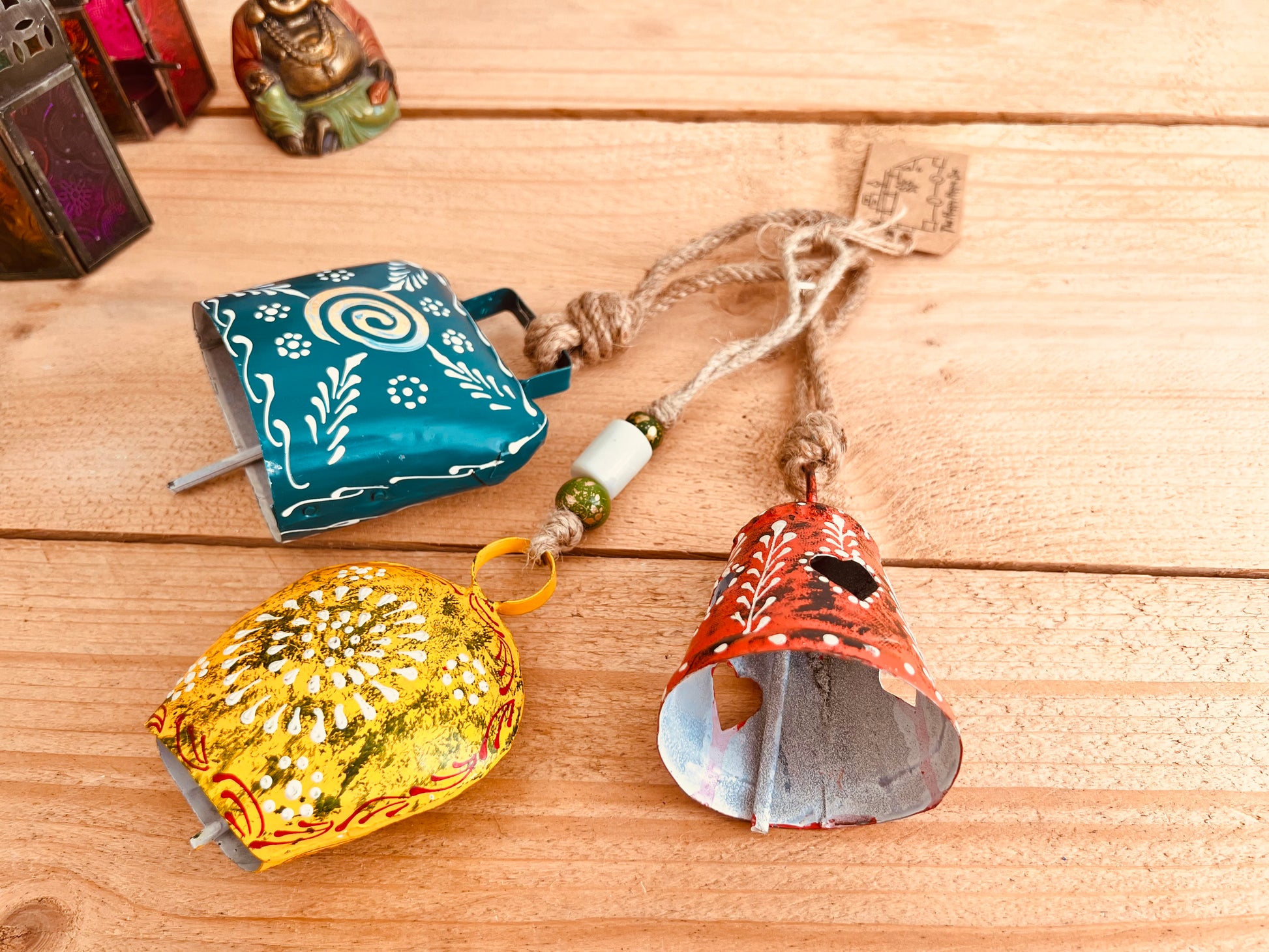 a set of three metal hand painted Indian hanging bells in three different sizes, jute twine hanging cow bell wind chimes in three mixed sizes, yellow, red & blue metal painted bells, handmade, fair trade & ethically sourced hippie boho home decor. 