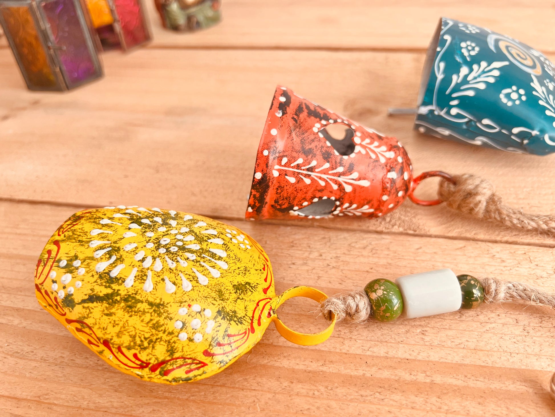 a set of three metal hand painted Indian hanging bells in three different sizes, jute twine hanging cow bell wind chimes in three mixed sizes, yellow, red & blue metal painted bells, handmade, fair trade & ethically sourced hippie boho home decor. 