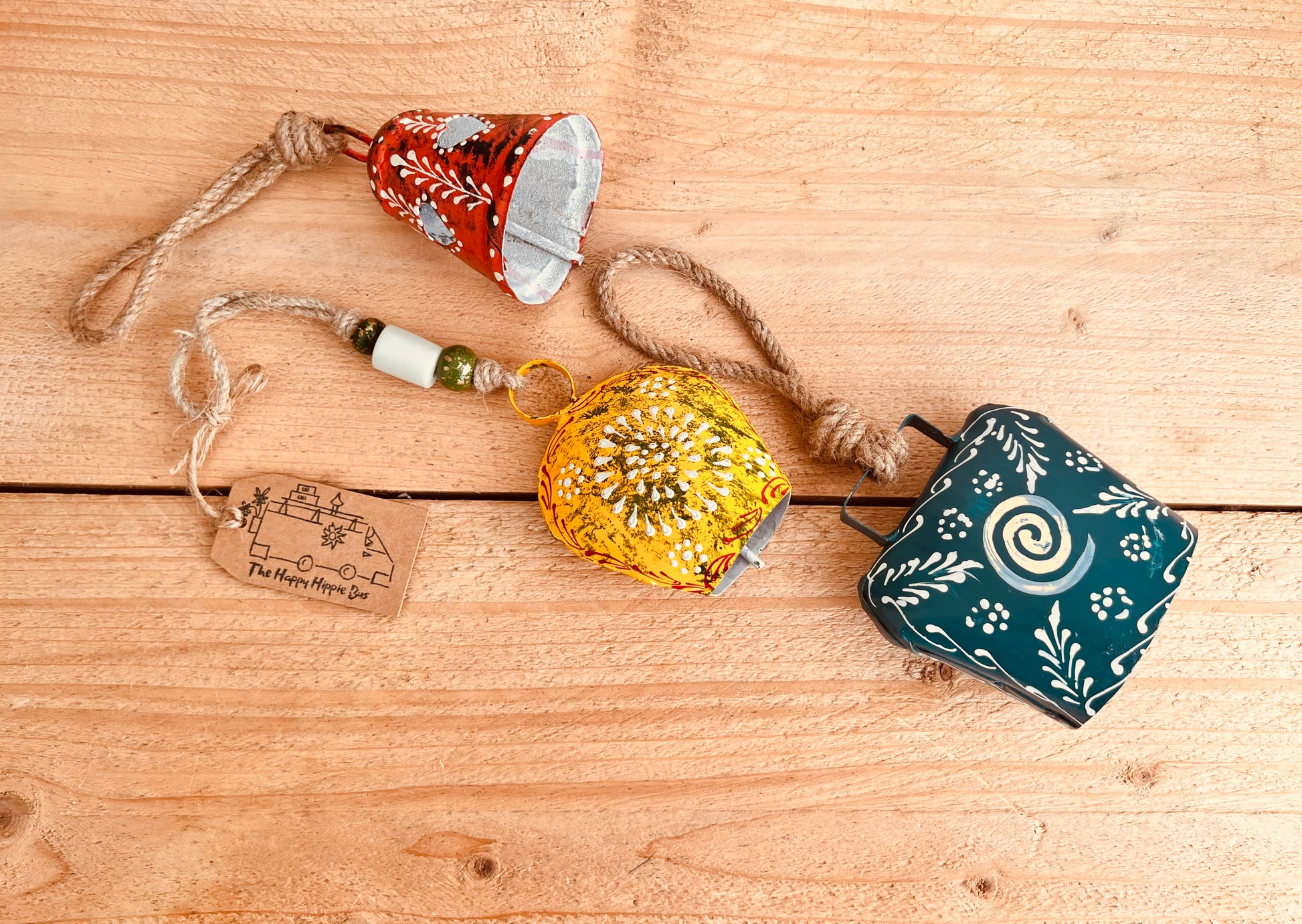 a set of three metal hand painted Indian hanging bells in three different sizes, jute twine hanging cow bell wind chimes in three mixed sizes, yellow, red & blue metal painted bells, handmade, fair trade & ethically sourced hippie boho home decor. 