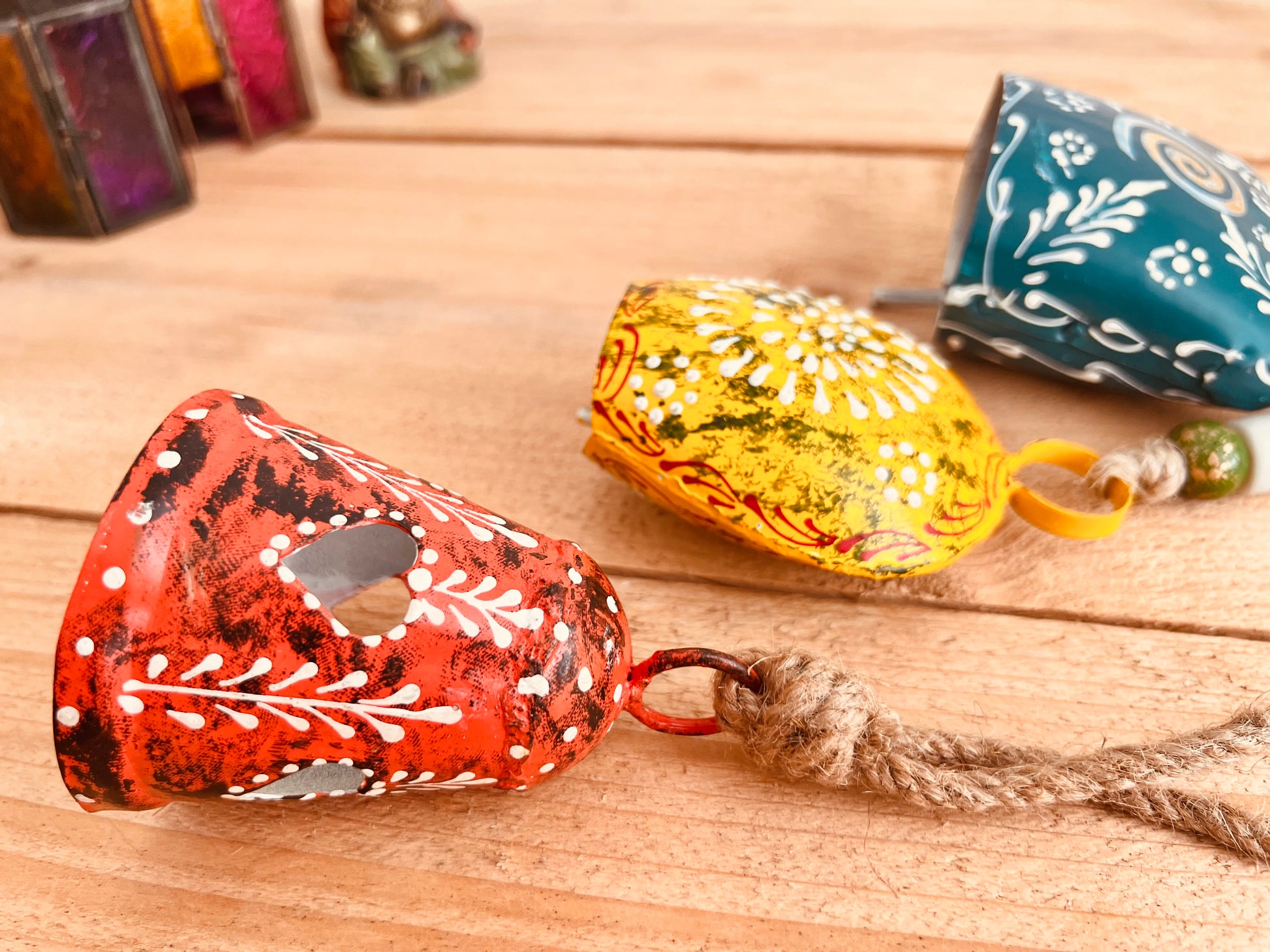 a set of three metal hand painted Indian hanging bells in three different sizes, jute twine hanging cow bell wind chimes in three mixed sizes, yellow, red & blue metal painted bells, handmade, fair trade & ethically sourced hippie boho home decor. 