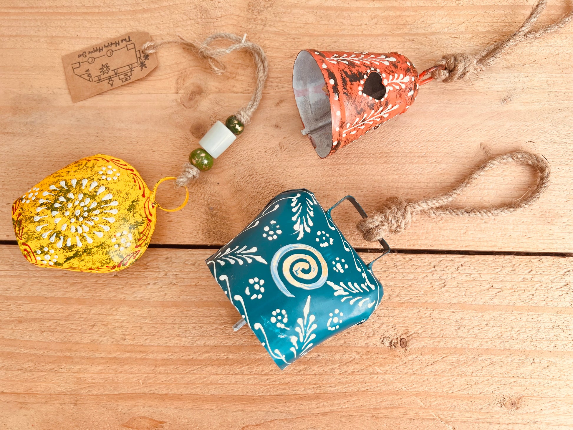a set of three metal hand painted Indian hanging bells in three different sizes, jute twine hanging cow bell wind chimes in three mixed sizes, yellow, red & blue metal painted bells, handmade, fair trade & ethically sourced hippie boho home decor. 